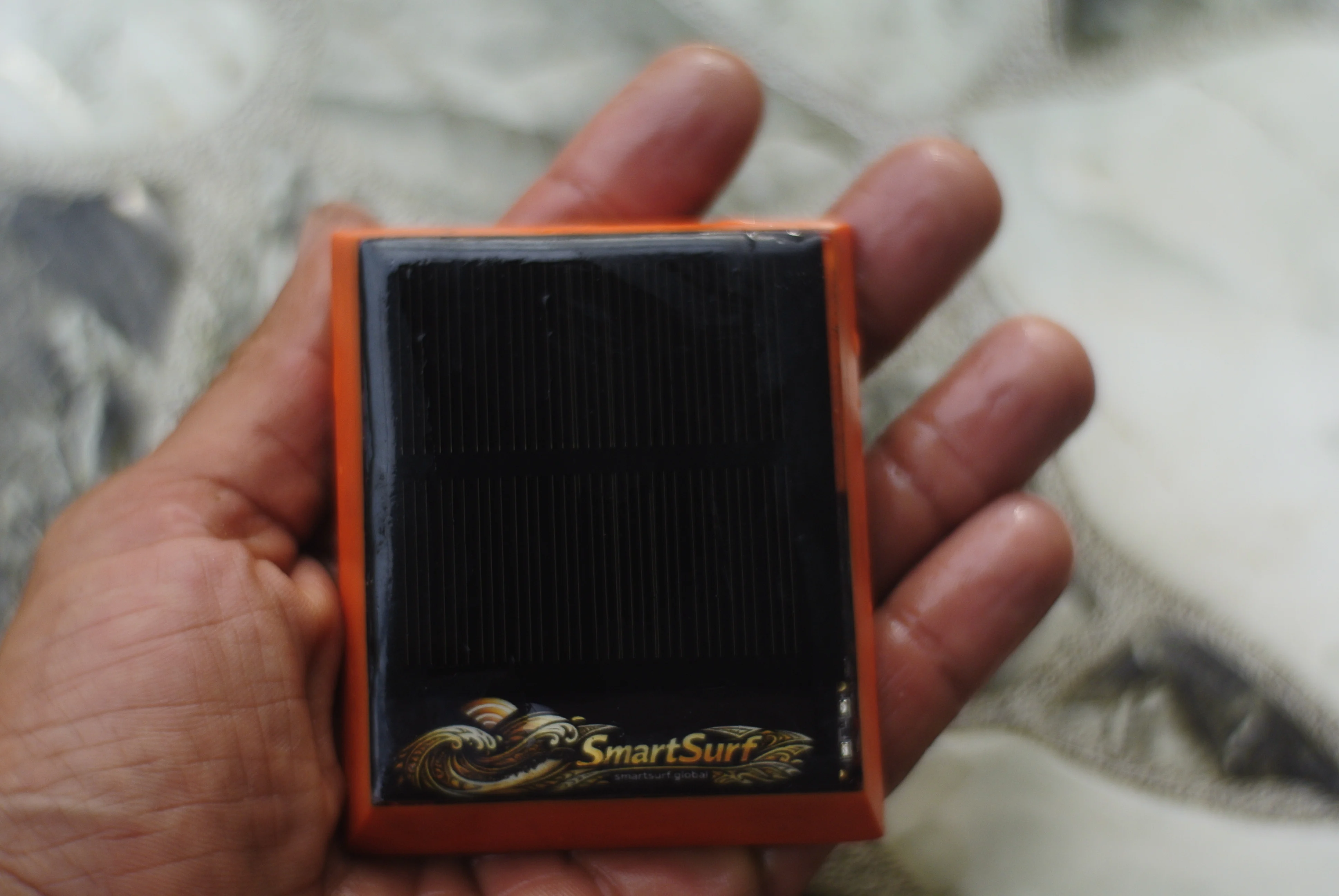 An orange SmartSurf prototype tracker with a solar panel, held in a rider’s hand